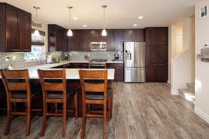Una cocina moderna con armarios de madera oscura, electrodomésticos de acero inoxidable y una isla central con taburetes de bar.