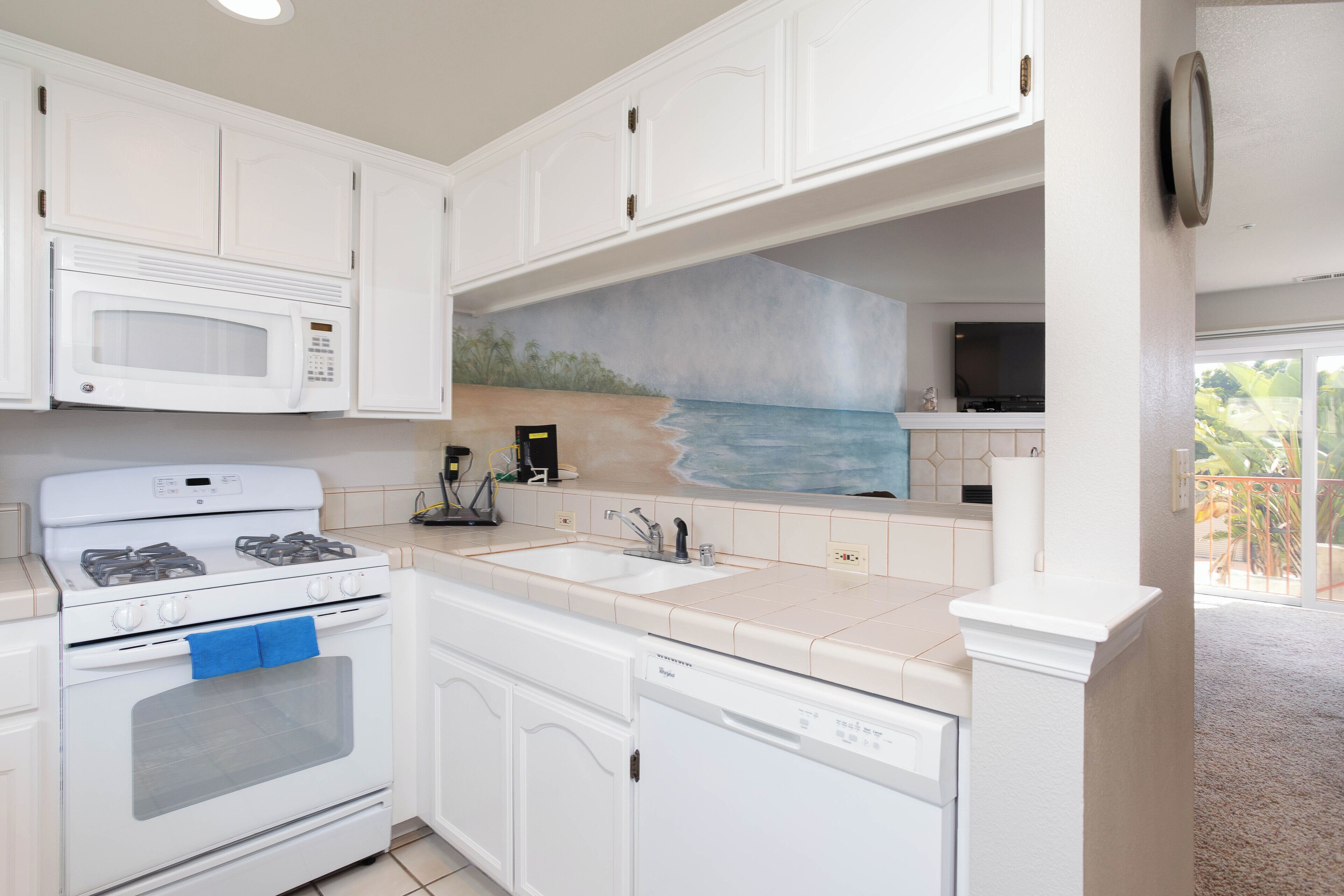 A kitchen with white cabinets, a microwave, stove, sink, and dishwasher.