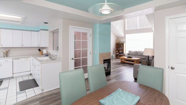 Een moderne keuken met witte kasten, een eethoek met een houten tafel en stoelen, en een woonkamer met een bank en een open haard.