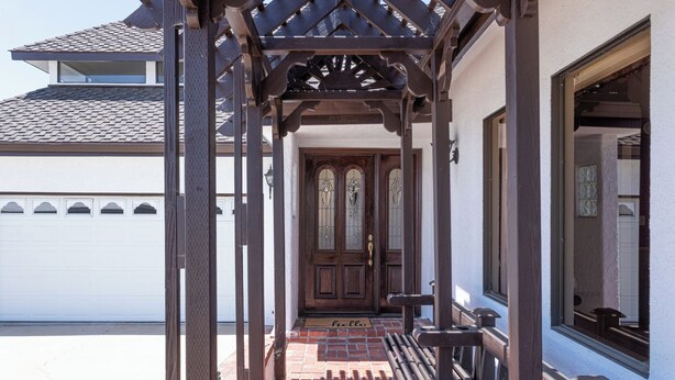 Eine Holzveranda mit einer Bank, einer Tür mit Buntglas und einer weißen Wand im Hintergrund.