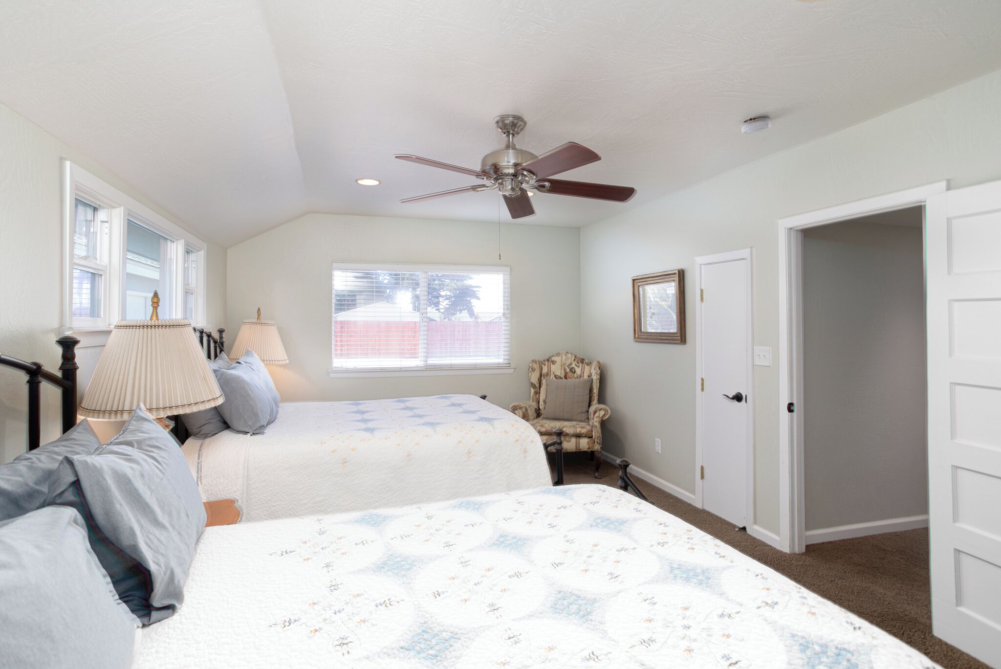 A bedroom with two beds, a ceiling fan, a chair, and a window.