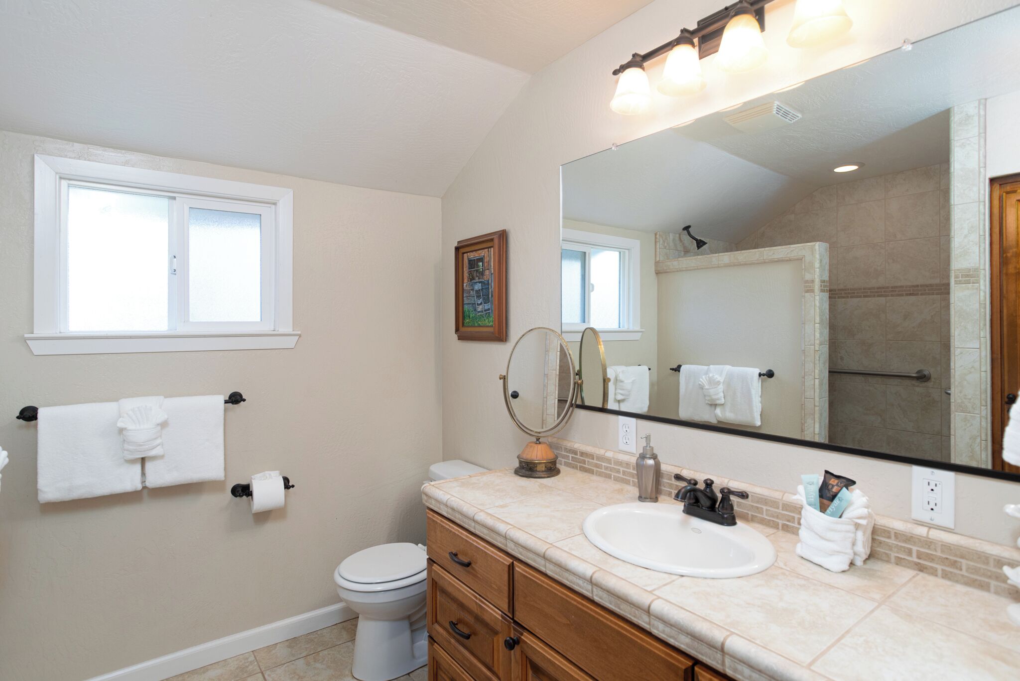 A bathroom with a toilet, sink, vanity, and a large mirror.