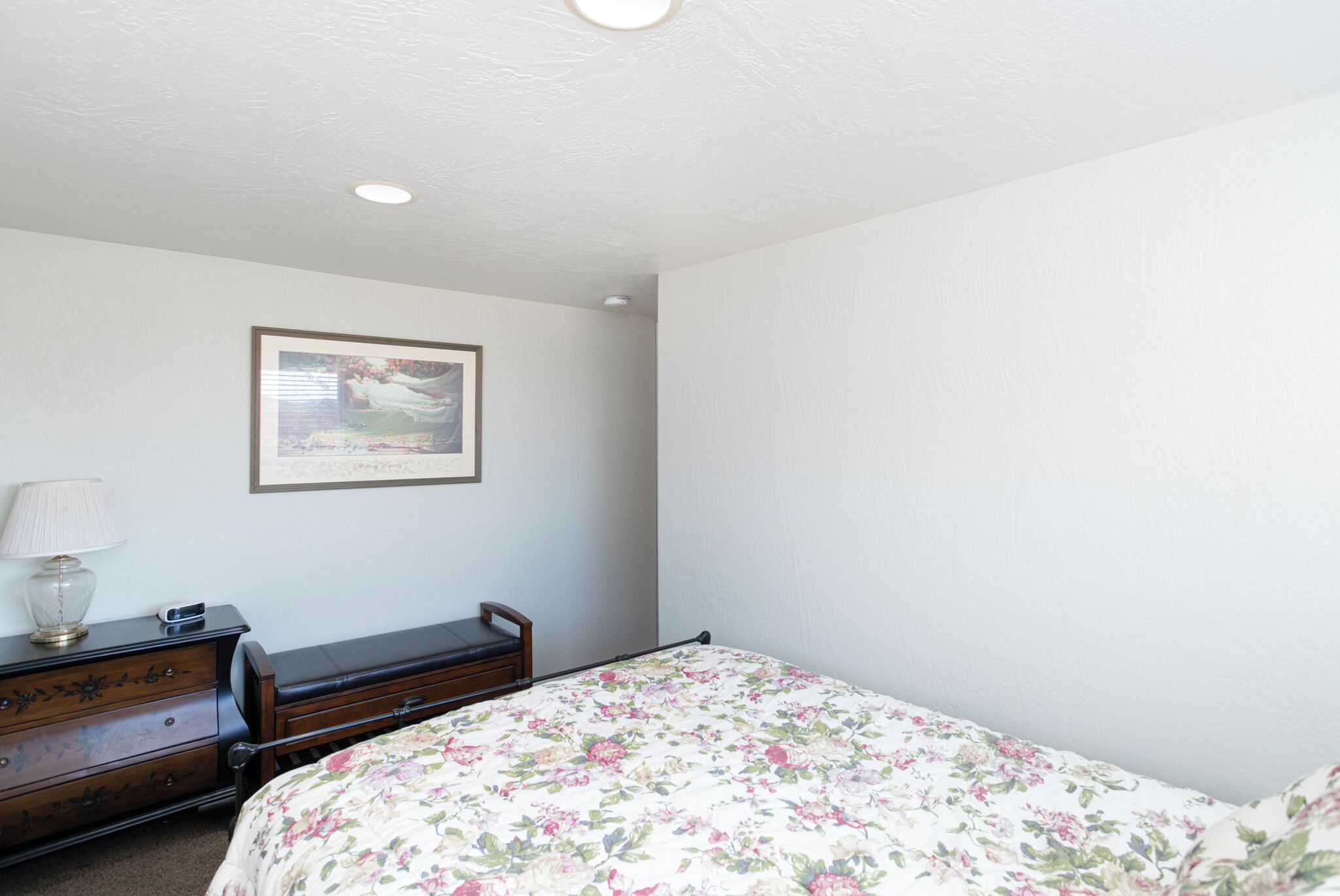 A bedroom with a bed, dresser, lamp, and framed picture on the wall.