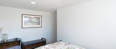A bedroom with a bed, dresser, lamp, and framed picture on the wall.