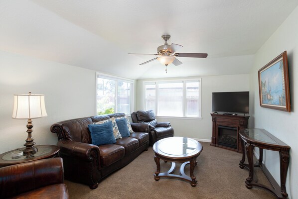 A living room with a brown leather sofa, a glass coffee table, a ceiling fan, a fireplace, and a television. - 2330 Paso Robles in Oceano (Oceano)