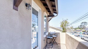 A balcony with a table and chairs, a window with blinds, and a view of a street with parked cars. - 1500 Brighton - STR00109 (Unknown)