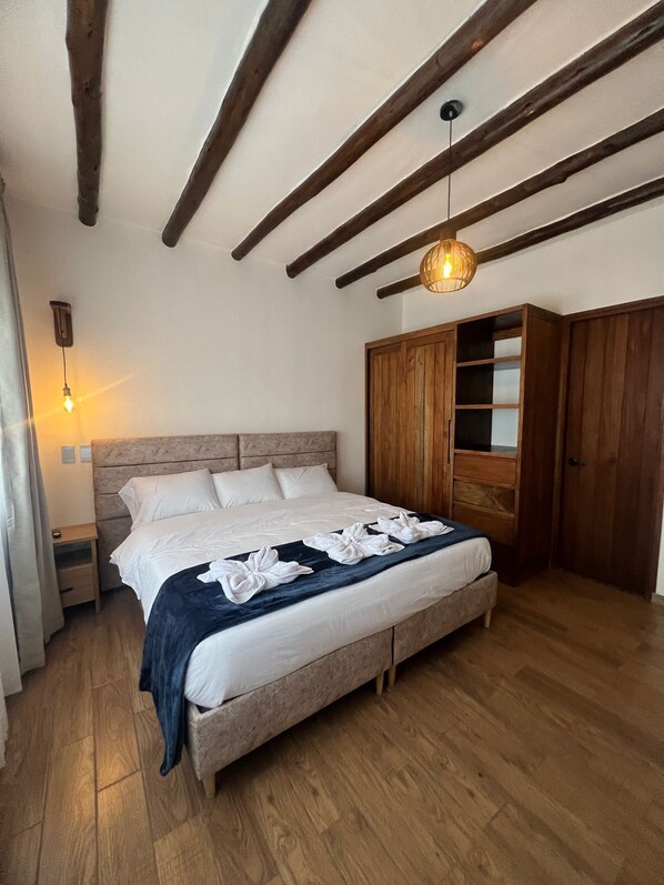 A bedroom with a wooden ceiling, a bed with white linens, a wooden wardrobe, and a hanging light fixture.