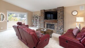 A living room with a stone fireplace, leather sofas, a flat-screen TV, and a bookshelf.