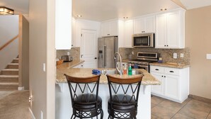 A modern kitchen with white cabinets, granite countertops, stainless steel appliances, and two bar stools.