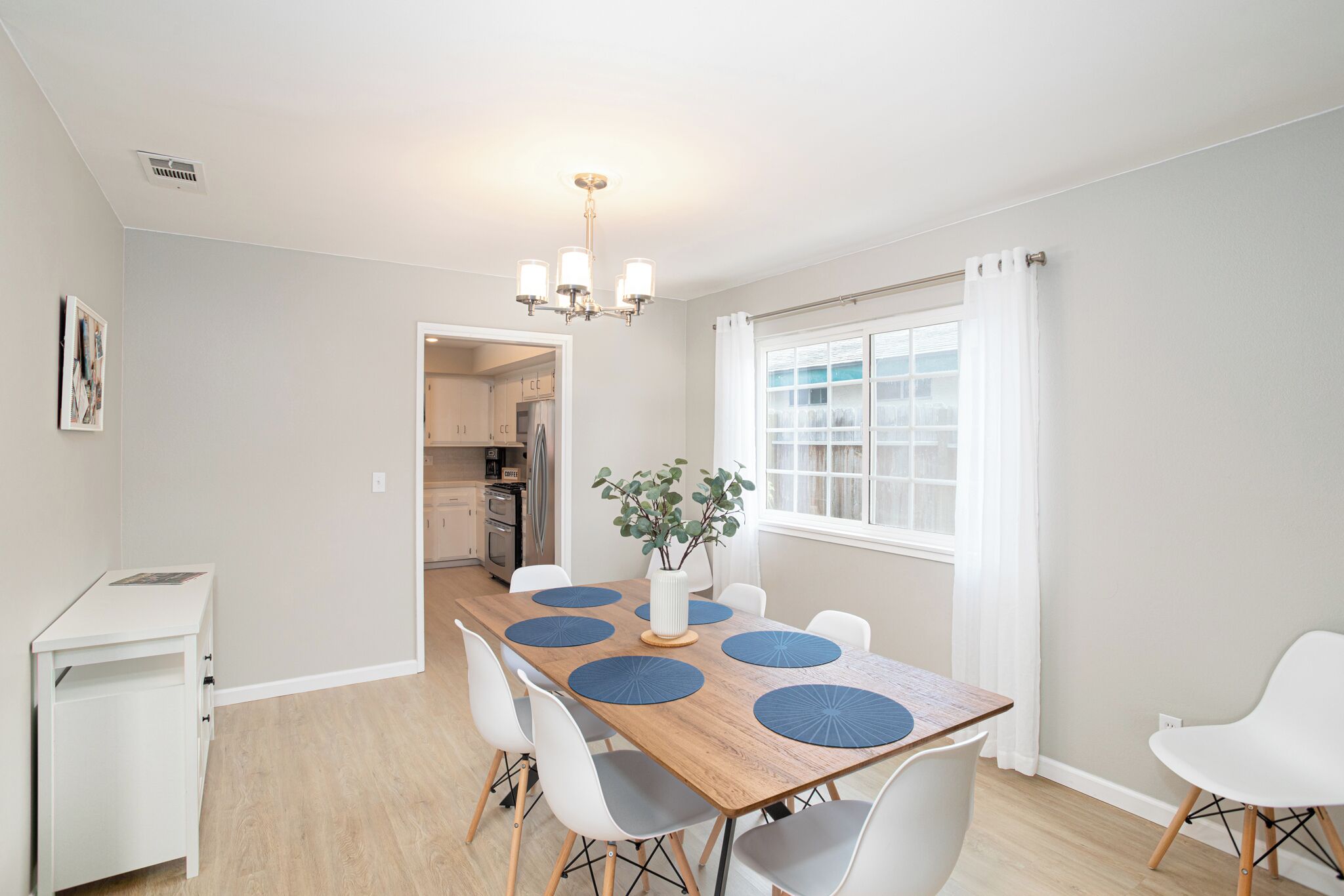 A dining area with a wooden table, white chairs, a vase with a plant, and a chandelier.