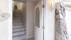 Un escalier menant à une porte dotée d’un panneau de verre, un mur de pierre avec une lanterne et un panneau indiquant une « zone d’accueil ».