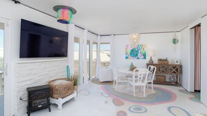 A cozy room with a fireplace, a dining table with chairs, a TV mounted on the wall, and a colorful rug.