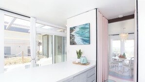 A modern kitchen with a white countertop, a painting of waves, and a dining area with a table and chairs.