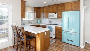 Una cocina con armarios de madera, un refrigerador turquesa, un microondas blanco y una isla de cocina con taburetes de bar.