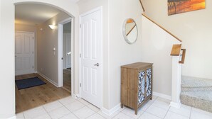 Un pasillo con una puerta de madera, un armario pequeño con diseños decorativos y un cuadro de un muelle en la pared.