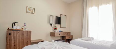 A hotel room with two beds, a wooden desk, a flat-screen TV, and a window with sheer curtains.