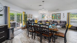 A modern living room with a dining area, featuring a chandelier, artwork, and a sofa.