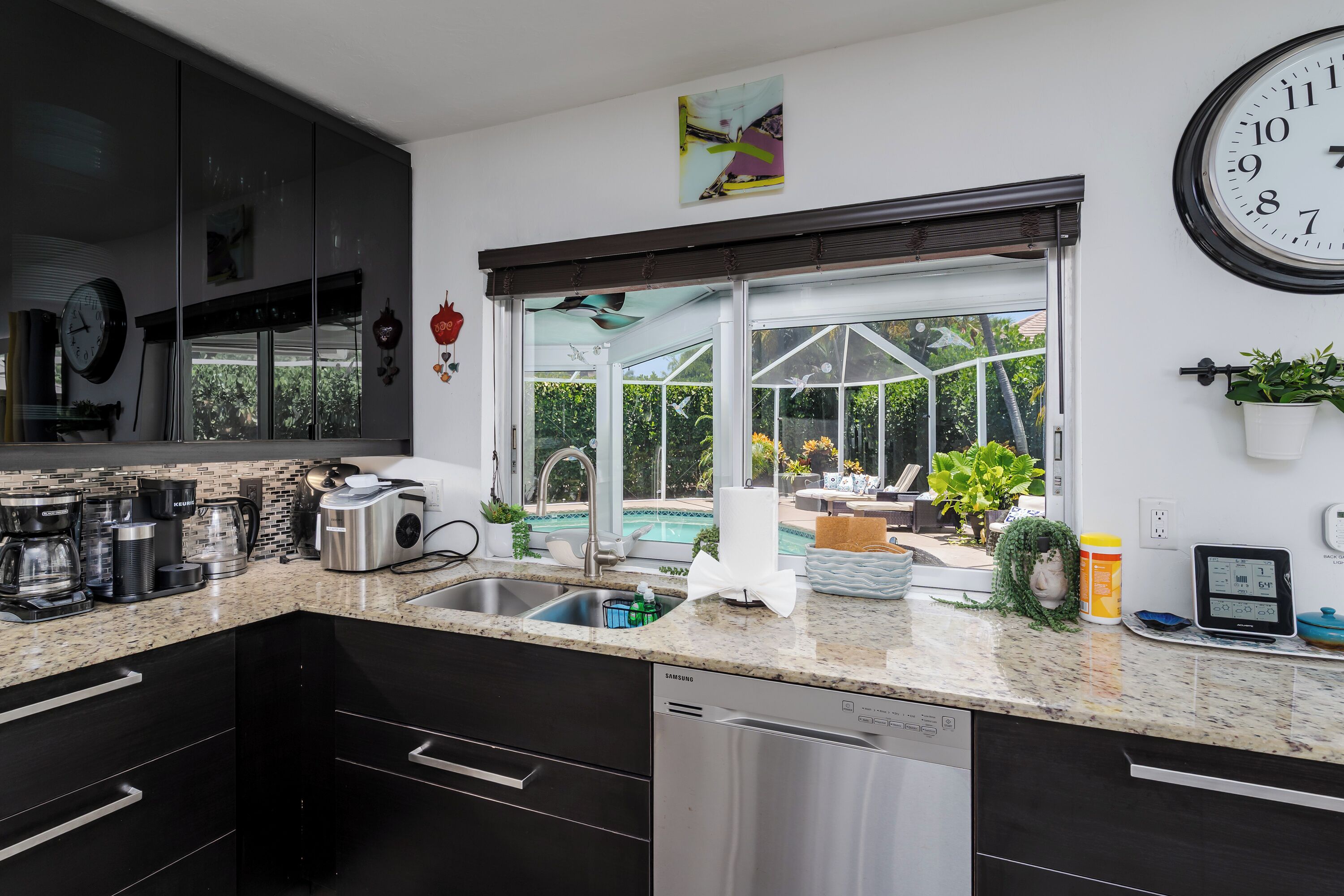 A modern kitchen with a dishwasher, coffee maker, and a large window overlooking a pool.