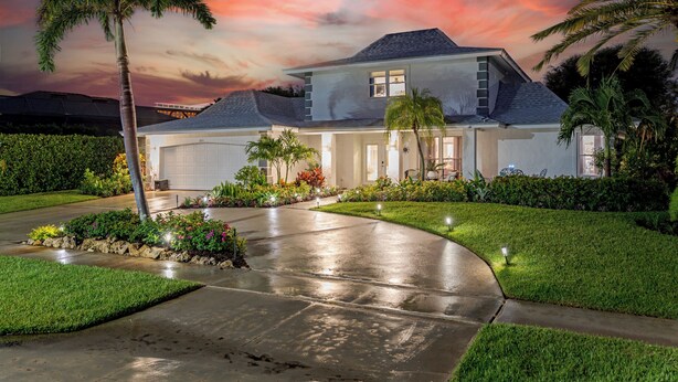 A two-story house with a garage, surrounded by well-maintained lawns and palm trees.
