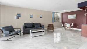 A modern living room with a grey sofa, a coffee table, a floor lamp, and a dining area with a table and chairs. - Bay Harbor Sunset Apt 2A (Bay Harbor Islands)