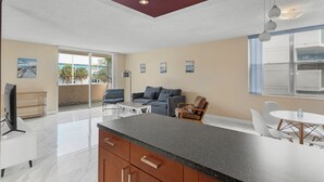 A modern kitchen with a black countertop, wooden cabinets, and a dining area with white chairs and a round table. - Bay Harbor Sunset Apt 2A (Bay Harbor Islands)
