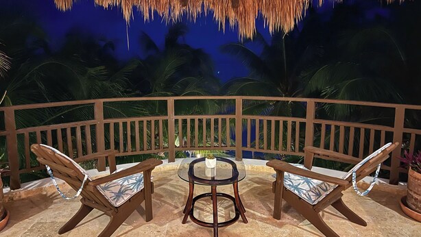 A thatched-roof outdoor area with two wooden chairs and a glass table, surrounded by a wooden railing and palm trees. - Beach front Paradise | Casa NFT Tulum-Soliman Bay (Tulum)