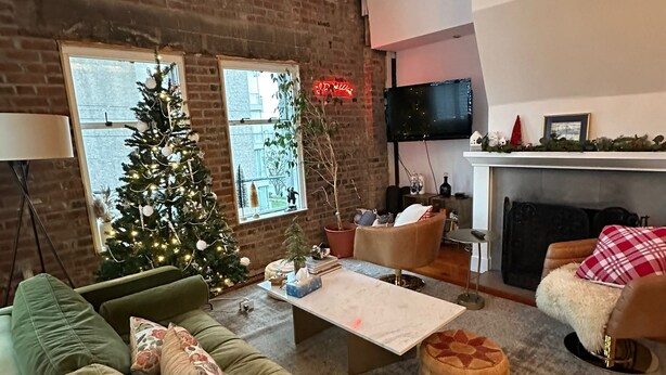 Ein gemütliches Wohnzimmer mit einem grünen Sofa, einem Couchtisch und einem Weihnachtsbaum. Ein Kamin ist vorhanden und ein Fernseher ist an der Wand befestigt.