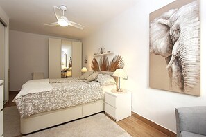 Un dormitorio con cama, mesitas de noche, ventilador de techo, espejo y un cuadro grande de un elefante en la pared.