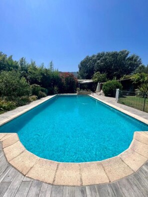 A rectangular swimming pool with a clear blue water surface, surrounded by a stone deck and bordered by a low stone wall.