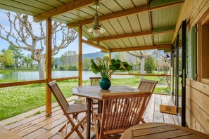 A wooden deck with a table and chairs, a hanging light fixture, and a view of a lake and trees.
