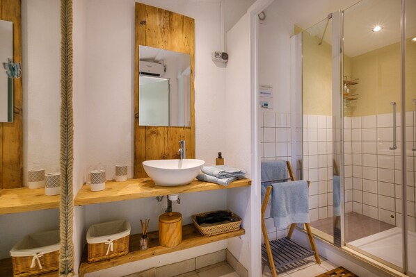 A bathroom with a wooden vanity, a white sink, a mirror, a glass shower enclosure, and a towel rack.