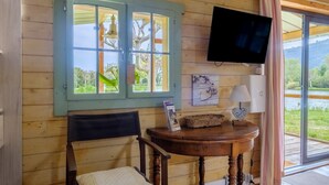 Ein Zimmer aus Holz mit einem Bett, einem Tisch mit Lampe, einem Fernseher und einem Fenster mit Vorhängen.