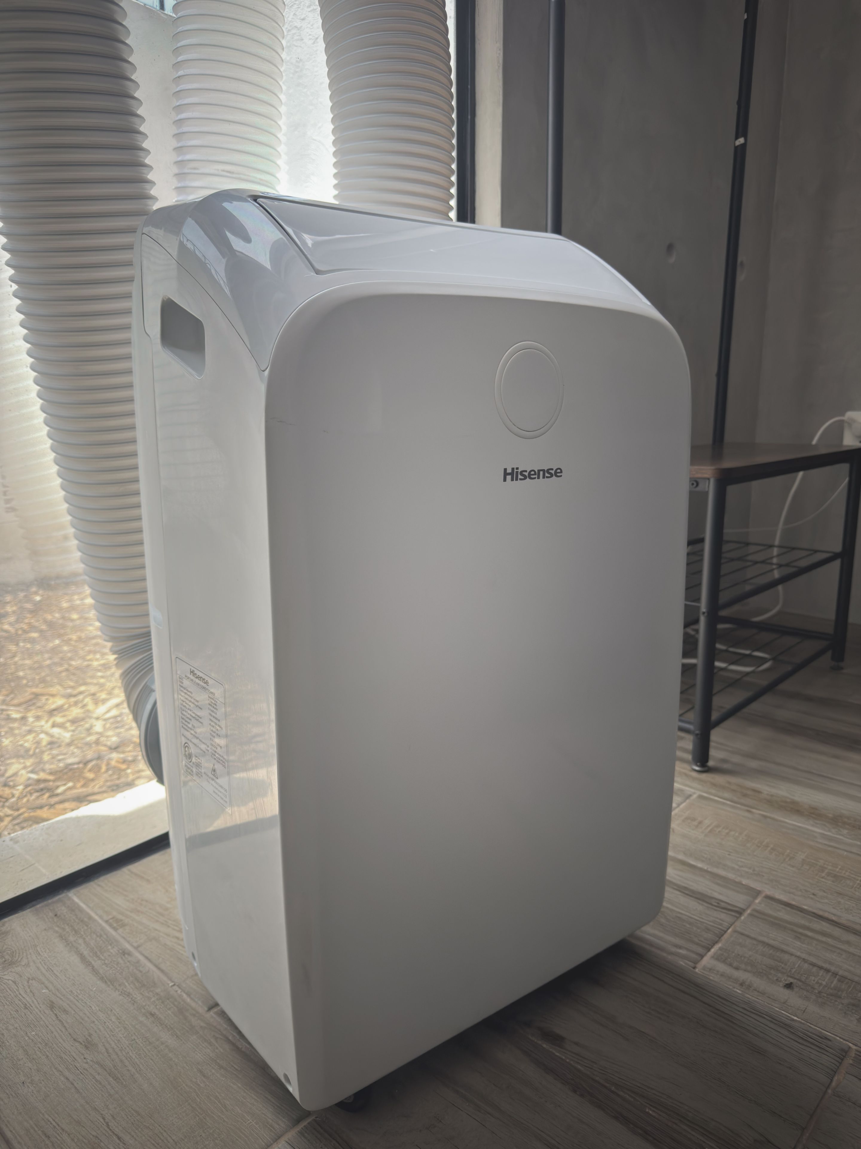 A white Hisense air purifier in a room with a window and a metal chair.