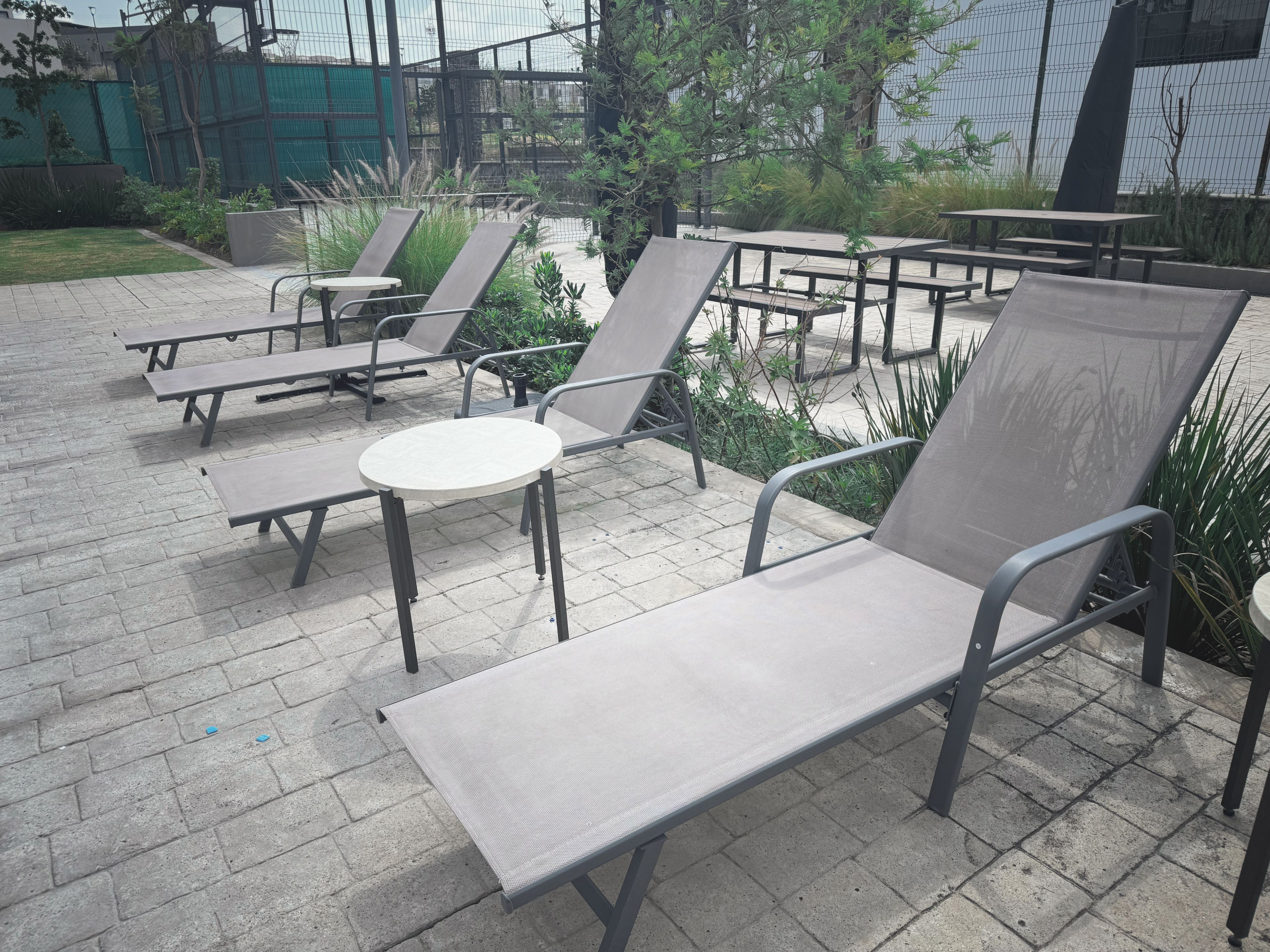 Espace extérieur aménagé avec des tables et des chaises, entouré de verdure et délimité par une clôture.