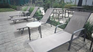 Espace extérieur aménagé avec des tables et des chaises, entouré de verdure et délimité par une clôture.