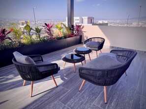 Una terrazza sul tetto con mobili in vimini, un tavolino rotondo e vista sulla città.