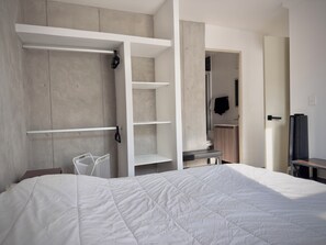 Une chambre à coucher avec un lit, une armoire, un bureau et une salle de bain visible à travers une porte ouverte.