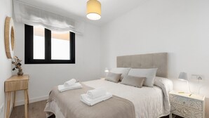 A bedroom with a bed, bedside table, lamp, and a window with a curtain.