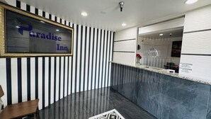 Un área de recepción con pared a rayas blancas y negras, piso de mármol y un cartel enmarcado que dice "Paradise Inn".