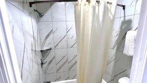 Un baño con ducha, inodoro y un rollo de papel higiénico en el suelo.