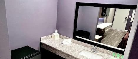 A bathroom with a marble countertop, a sink, a mirror, and a trash bin.