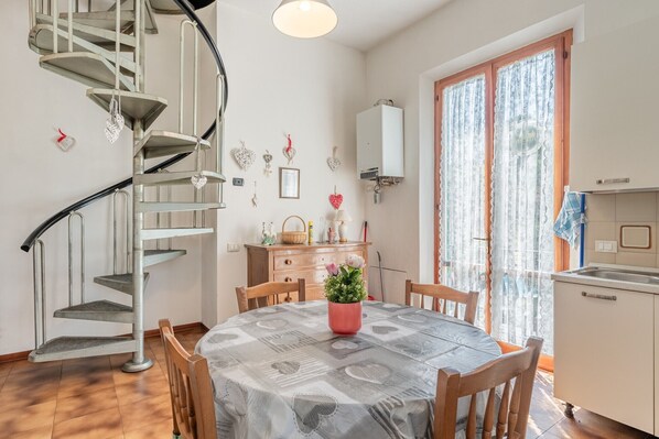 Un espace repas comprenant une table ronde, des chaises, un escalier en colimaçon, une cuisine et une fenêtre avec des rideaux.