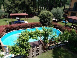 Une piscine entourée d’une clôture en bois, avec une pelouse et des arbres en arrière-plan.