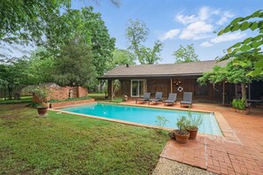 A backyard with a swimming pool, a brick patio, and a wooden deck.