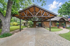 A covered outdoor area with a wooden structure, a paved walkway, and a building with a flag.
