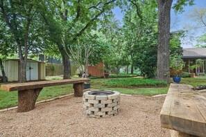 A backyard with a fire pit, wooden benches, and a shed.