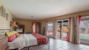 Ein Schlafzimmer mit einem Bett, einem Holzschrank, einem Nachttisch, einem Fenster mit Vorhängen und Blick ins Freie.