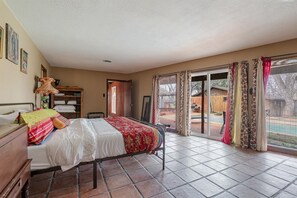 Ein Schlafzimmer mit einem Bett, einem Holzschrank, einem Nachttisch, einem Fenster mit Vorhängen und Blick ins Freie.