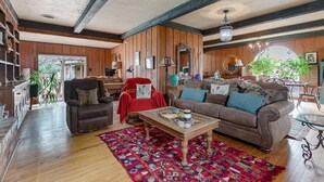 Ein geräumiges Wohnzimmer mit Holzbalkendecke, einem braunen Ledersofa, einem roten Sessel und einem Glastisch.