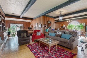 Ein geräumiges Wohnzimmer mit Holzbalkendecke, einem braunen Ledersofa, einem roten Sessel und einem Glastisch.